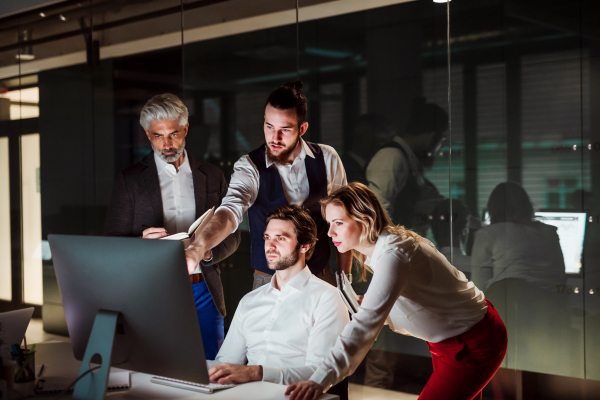 A group of business people in an office in the evening or at night, using computer.