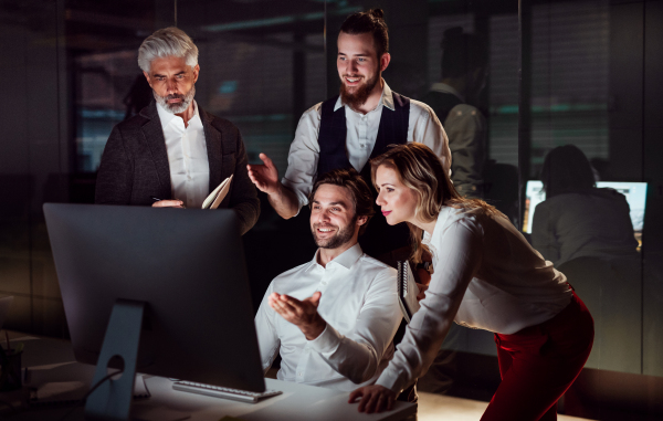 A group of business people in an office in the evening or at night, using computer.