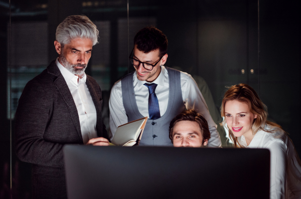 A group of business people in an office in the evening or at night, using computer.