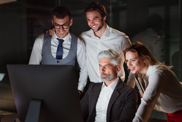 A group of business people in an office in the evening or at night, using computer.