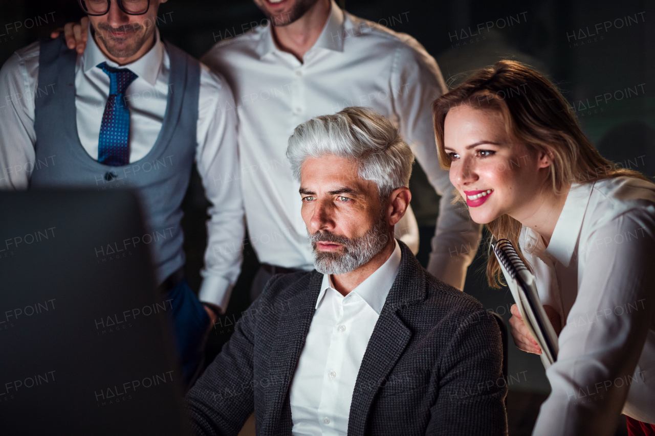 A group of business people in an office in the evening or at night, using computer.