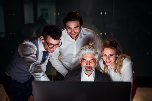 A group of business people in an office in the evening or at night, using computer.