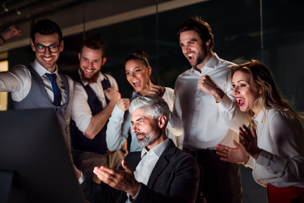 A group of business people with computer in an office in the evening or at night, expressing excitement.