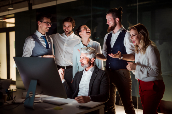 A group of business people with computer in an office in the evening, expressing excitement.