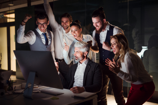 A group of business people with computer in an office in the evening or at night, expressing excitement.