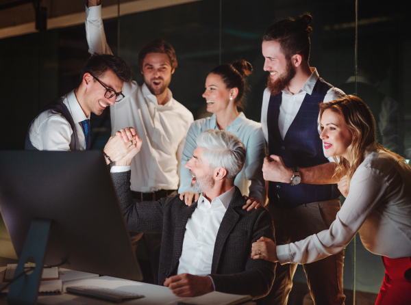 A group of business people with computer in an office in the evening or at night, expressing excitement.