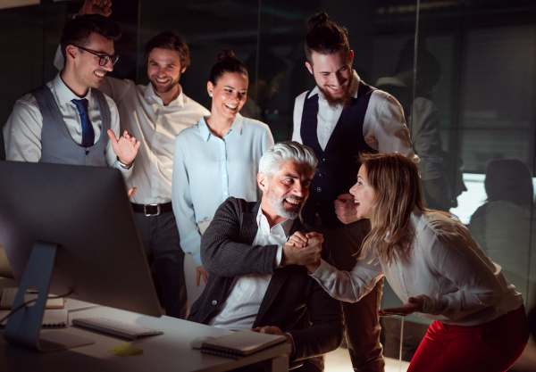 A group of business people with computer in an office in the evening, expressing excitement.