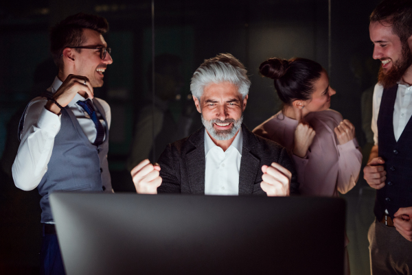 A group of business people with computer in an office in the evening, expressing excitement.