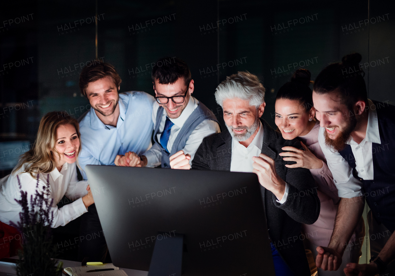 A group of business people with computer in an office in the evening, expressing excitement.