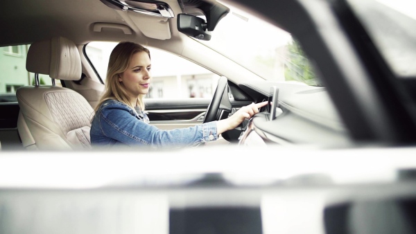 A young woman driver sitting in car, setting radio or navigation. Slow motion.