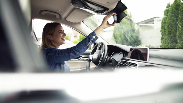 Young woman sitting in car, adjusting rear view mirror. Slow motion.