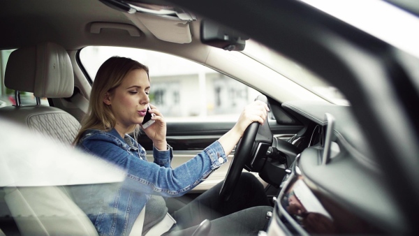 Young woman with smartphone sitting in car, making a phone call. Slow motion.