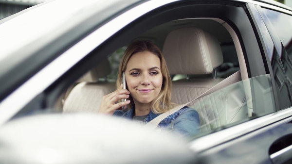 Young tired woman with smartphone sitting in car, making a phone call. Slow motion.