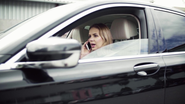 Young woman with smartphone sitting in car, making a phone call. Slow motion.