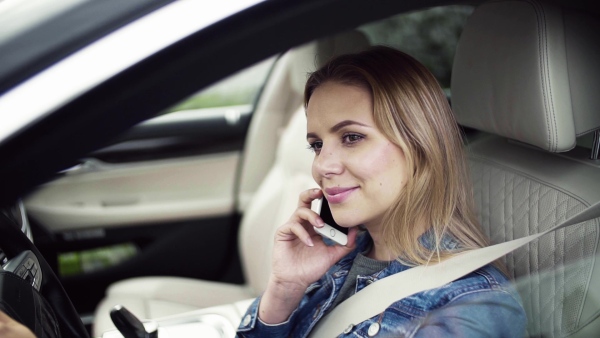 Young woman with smartphone sitting in car, making a phone call. Slow motion.