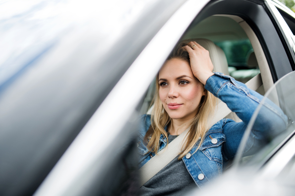 A bored young woman driver sitting in car, waiting.