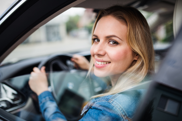 Beautiful young woman driver sitting in car, looking out.