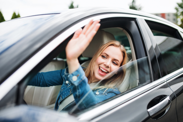 A young woman driver sitting in car, greeting somebody.