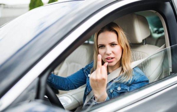 An angry young woman driver sitting in car, showing middle finger.