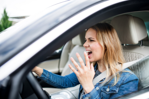 Angry young woman driver sitting in car, shouting when driving.