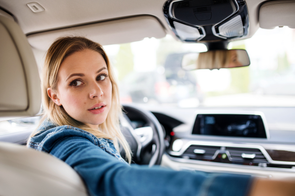 A young woman driver sitting in car, looking back.