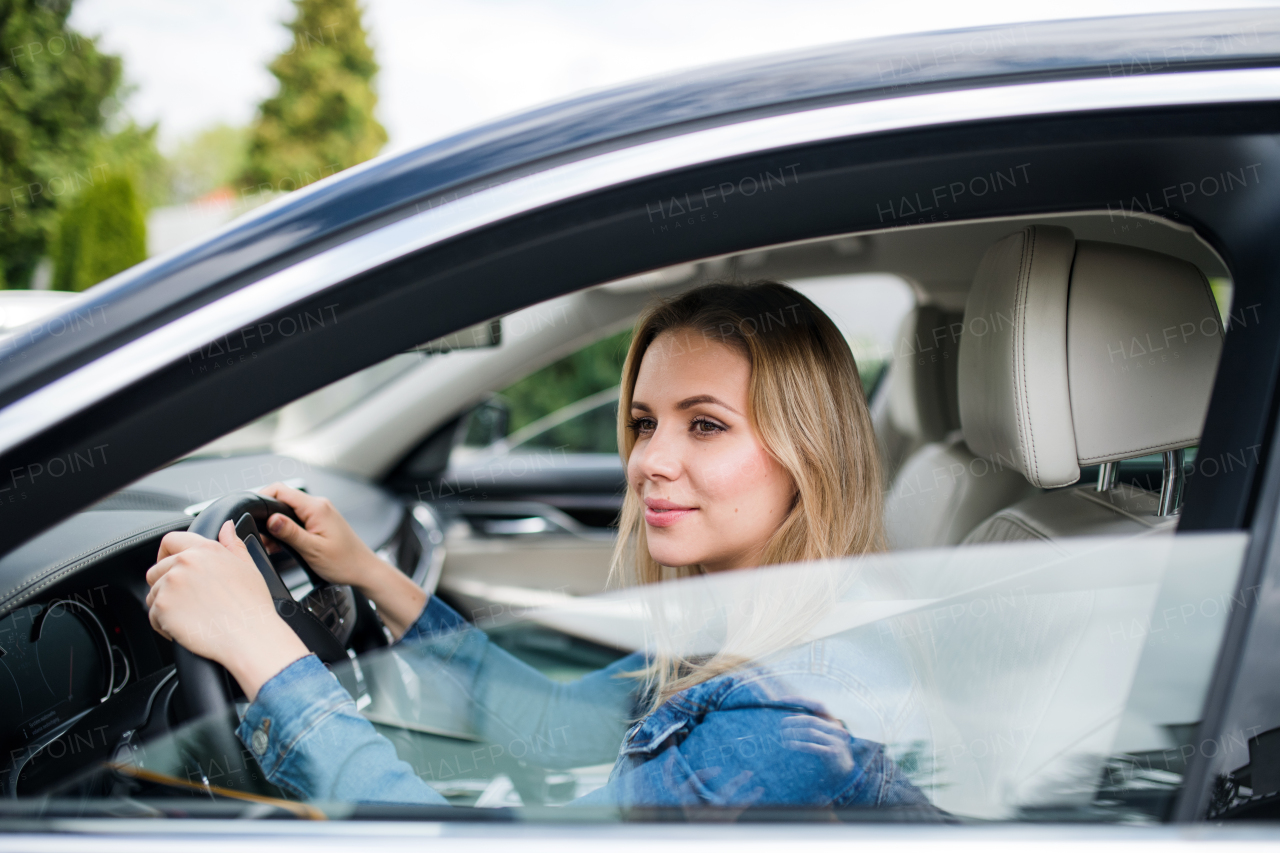 A happy young woman driver sitting in car, waiting.