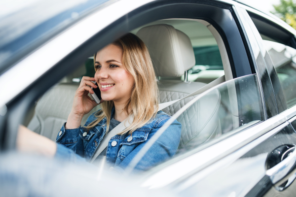 A young woman driver with smartphone sitting in car, making phone call.