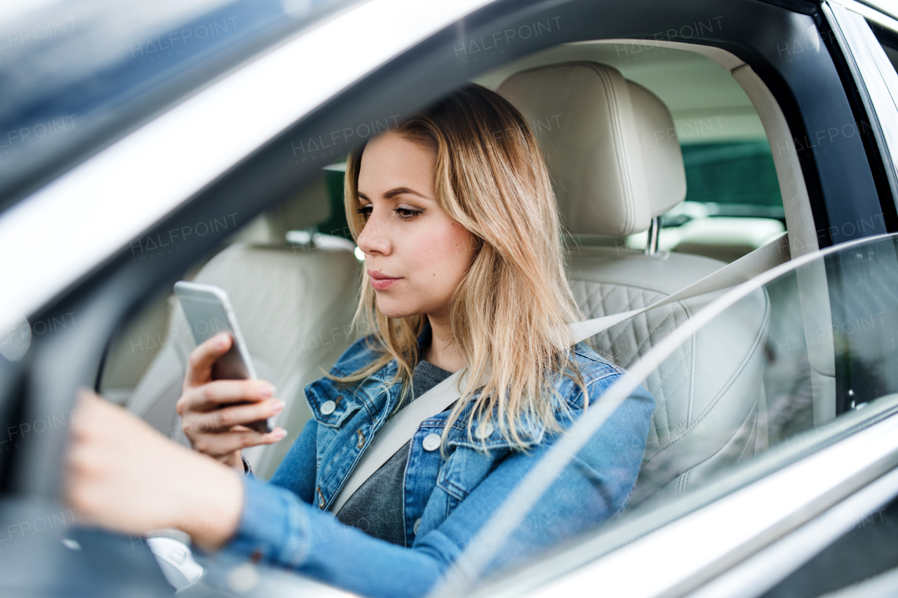 A young woman driver sitting in car, using smartphone.