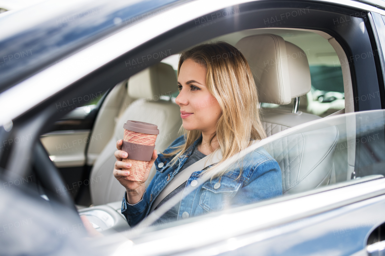 A young woman driver sitting in car, drinking coffee from paper cup.