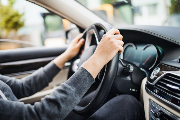 A midsection of arms of young woman driver sitting in car, driving.