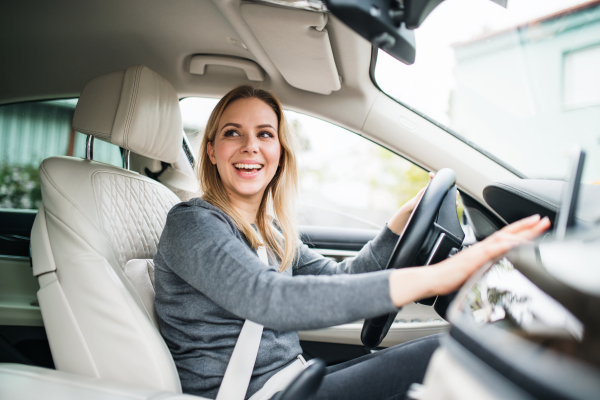 Happy young woman driver sitting in car, driving.