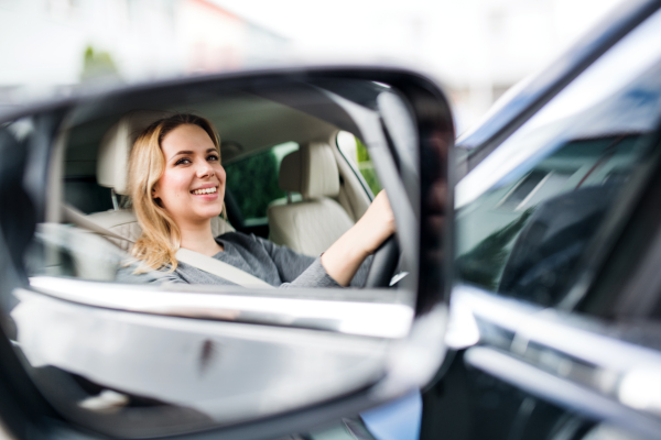 A mirror reflection of young woman driver sitting in car, driving.