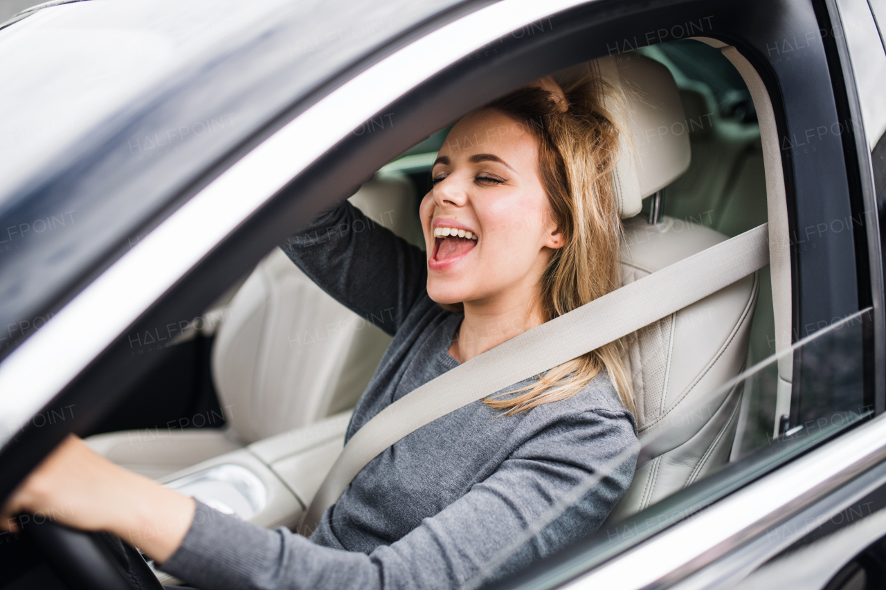 A cheerful young woman driver sitting in car, driving.