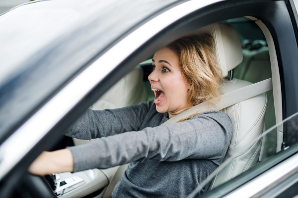 A shocked young woman driver sitting in car, involved in accident.