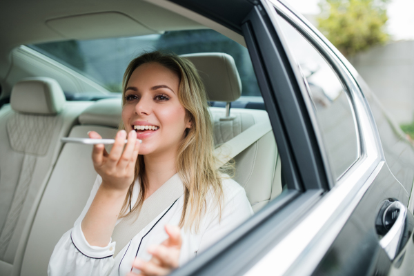 Business woman with smartphone and laptop sitting on back seats in taxi car, talking on the phone.