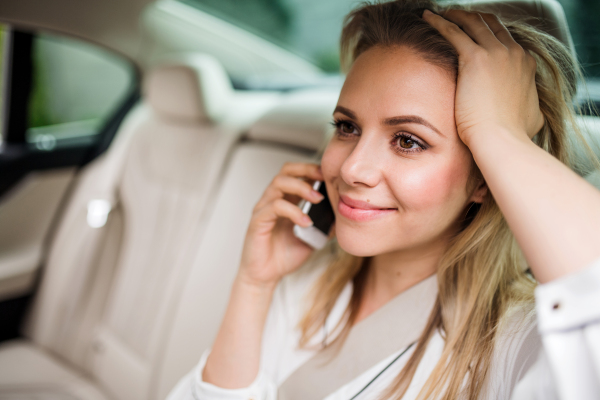 Business woman with smartphone sitting on back seats in taxi car, making phone call.