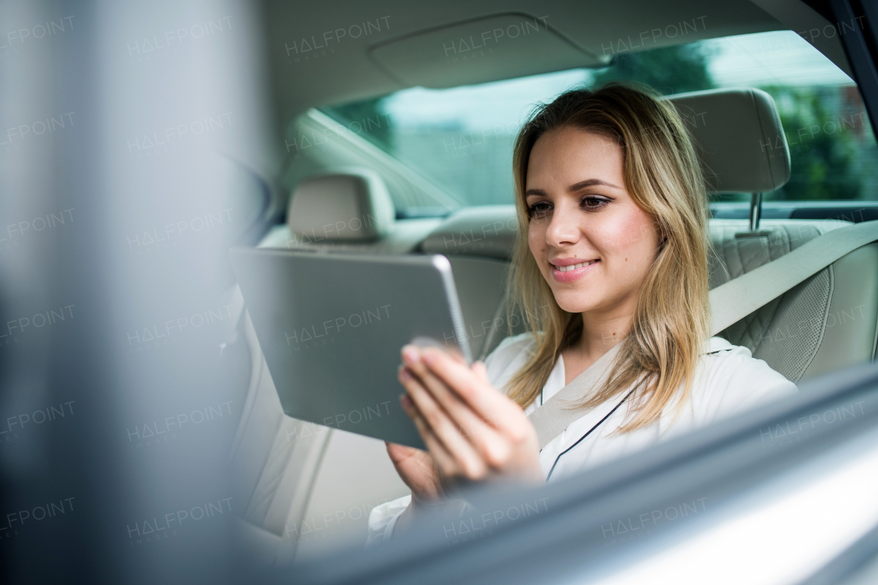 Young businesswoman with tablet sitting on back seats in taxi car, working.