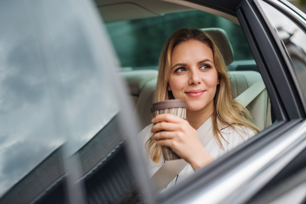 A business woman with coffee sitting on back seats in taxi car.