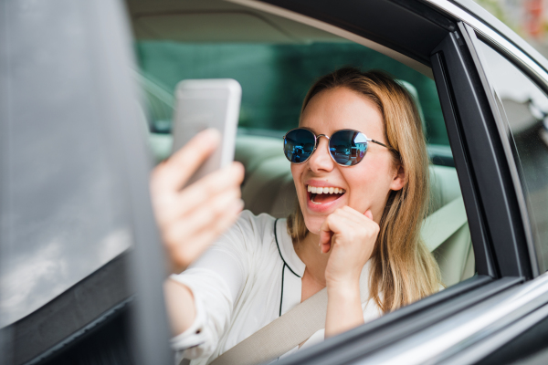 Business woman sitting on back seat in taxi car, taking selfie. Copy space.