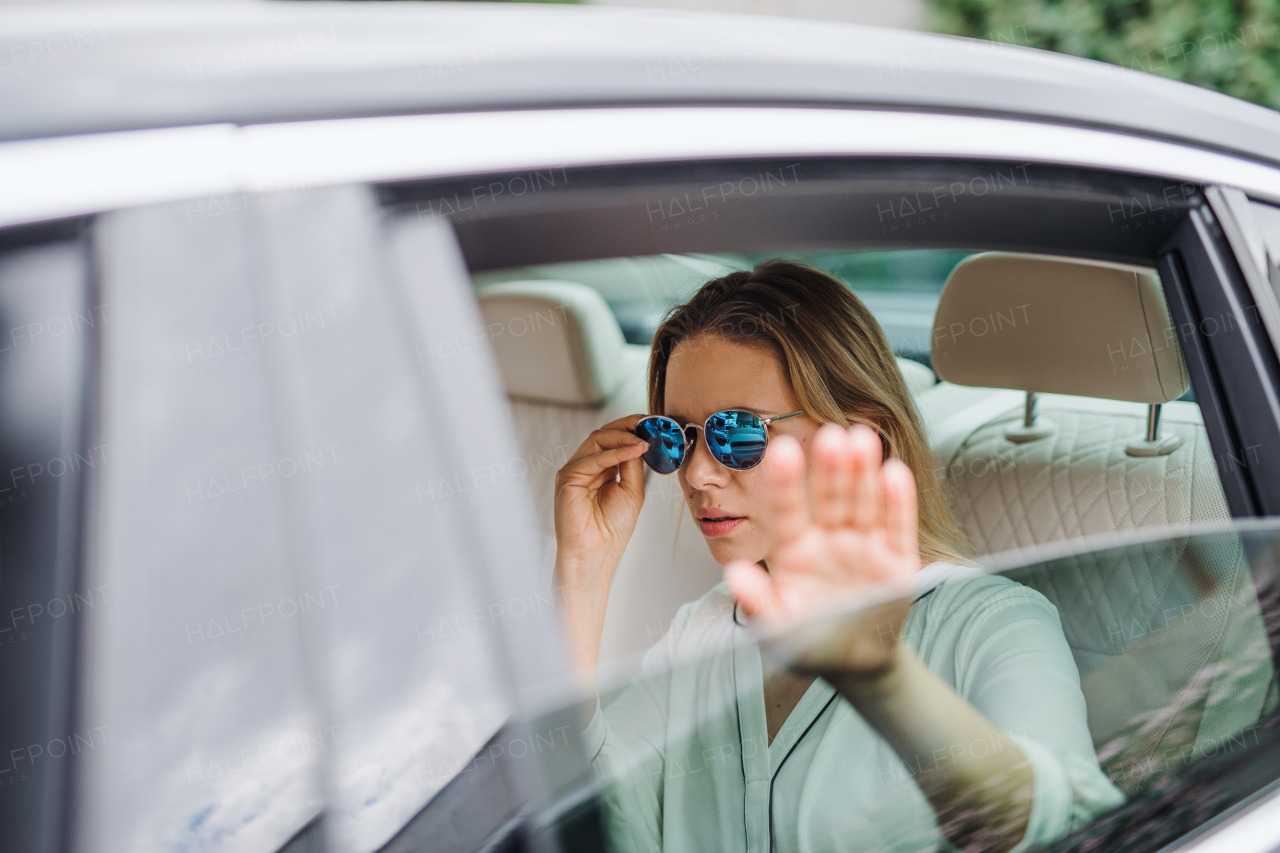 Young woman with sunglasses sitting on back seat of car, hiding face from paparazzi.