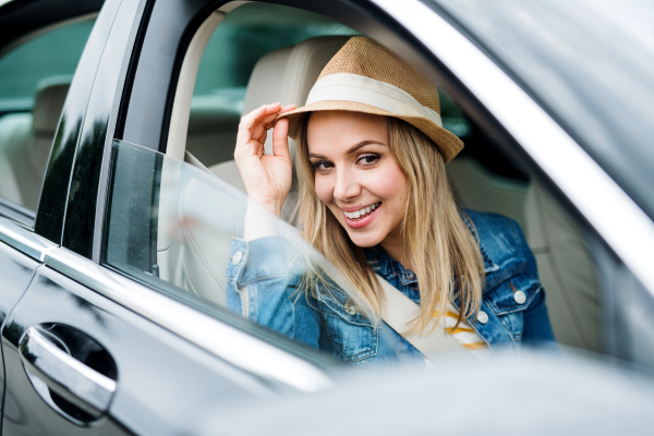 Beautiful young woman with hat sitting in car, looking out.