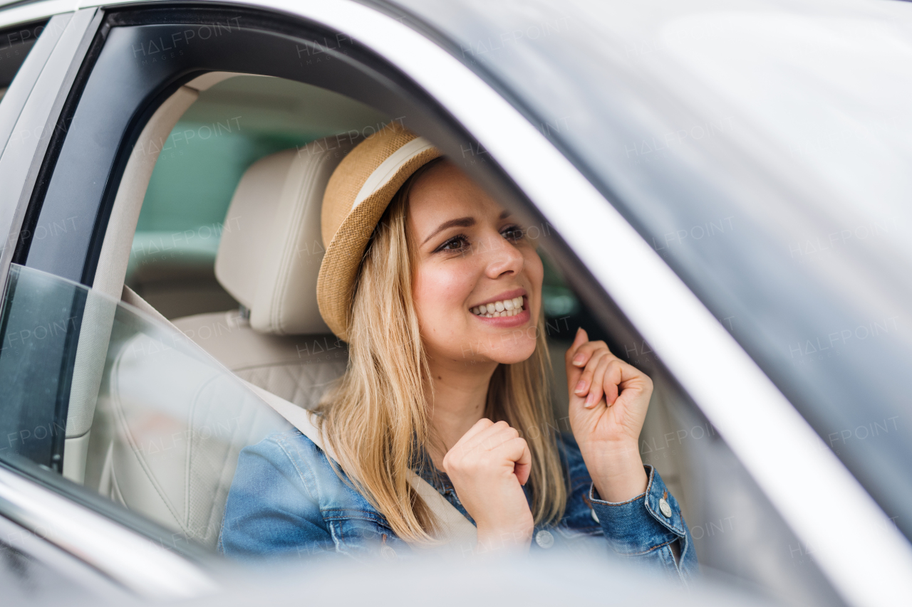 A young cheerful woman with hat sitting in car, listening to music and dancing.