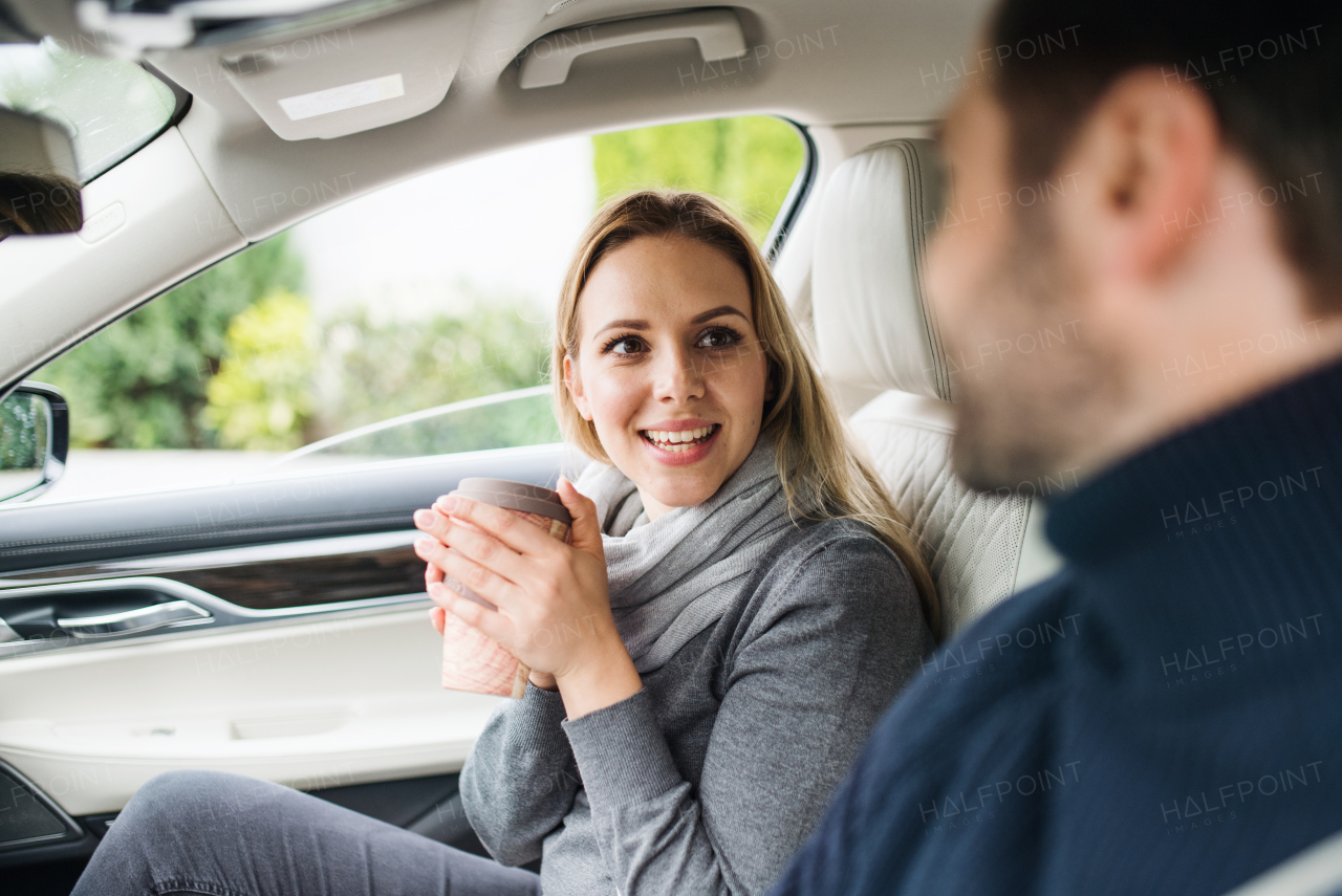 A happy young couple with coffee sitting in car, talking.