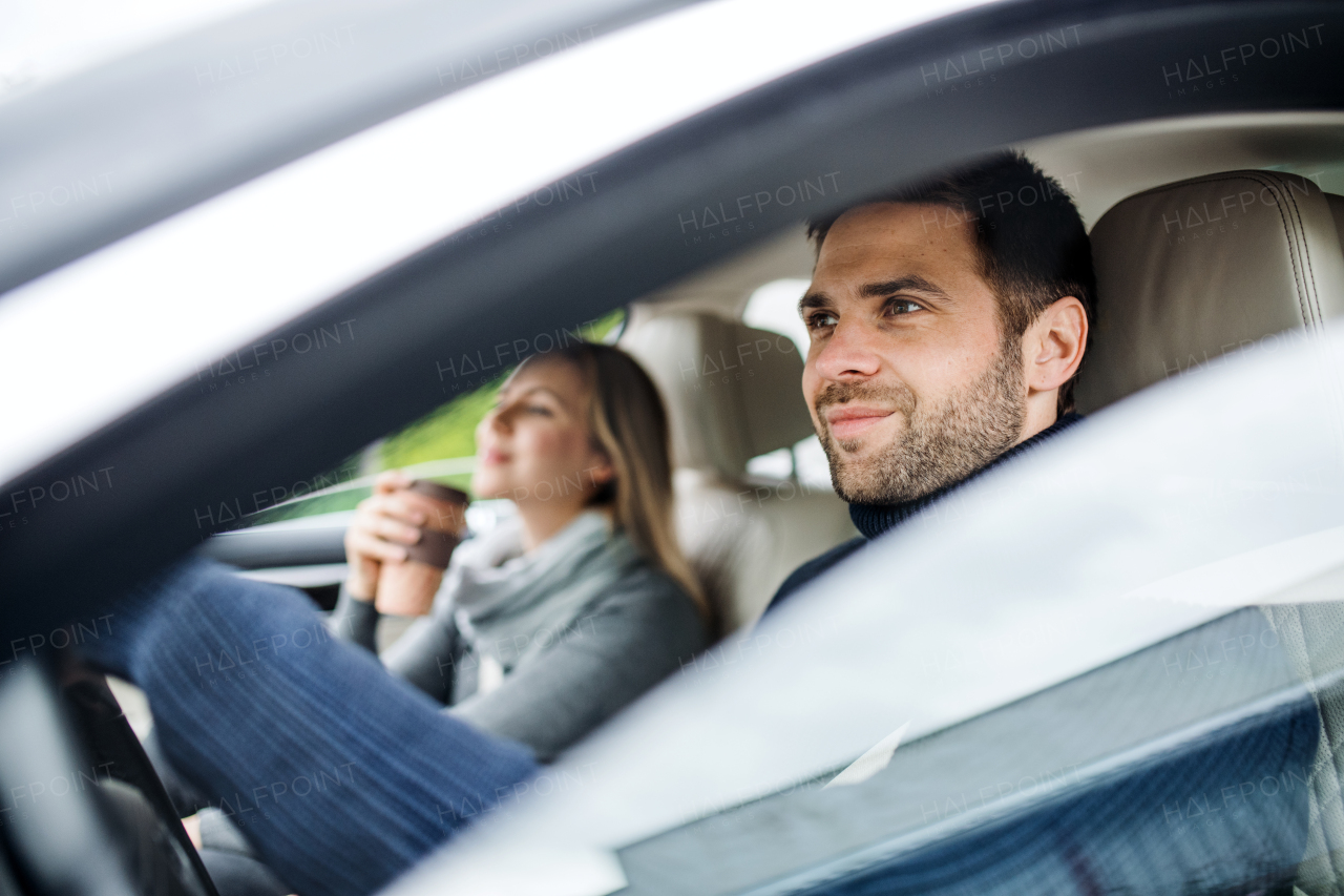 A happy young couple with coffee sitting in car, driving.