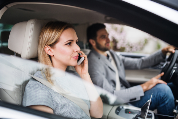 A happy young couple sitting in car, making a phone call.