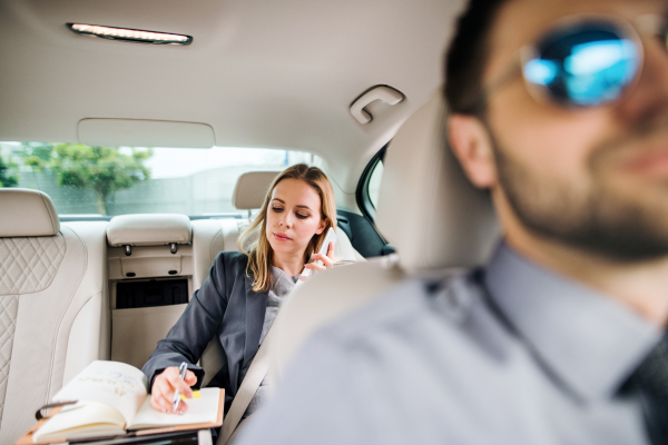 Business woman with smartphone sitting on back seat in taxi car, talking on the phone.