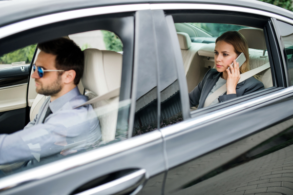 Businesswoman with driver sitting on back seat in taxi car, talking on the phone.