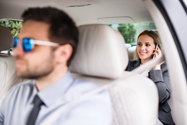 Business woman with smartphone sitting on back seats in taxi car, talking on the phone.