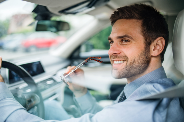 A young businessman with shirt sitting in car. Shot through glass.