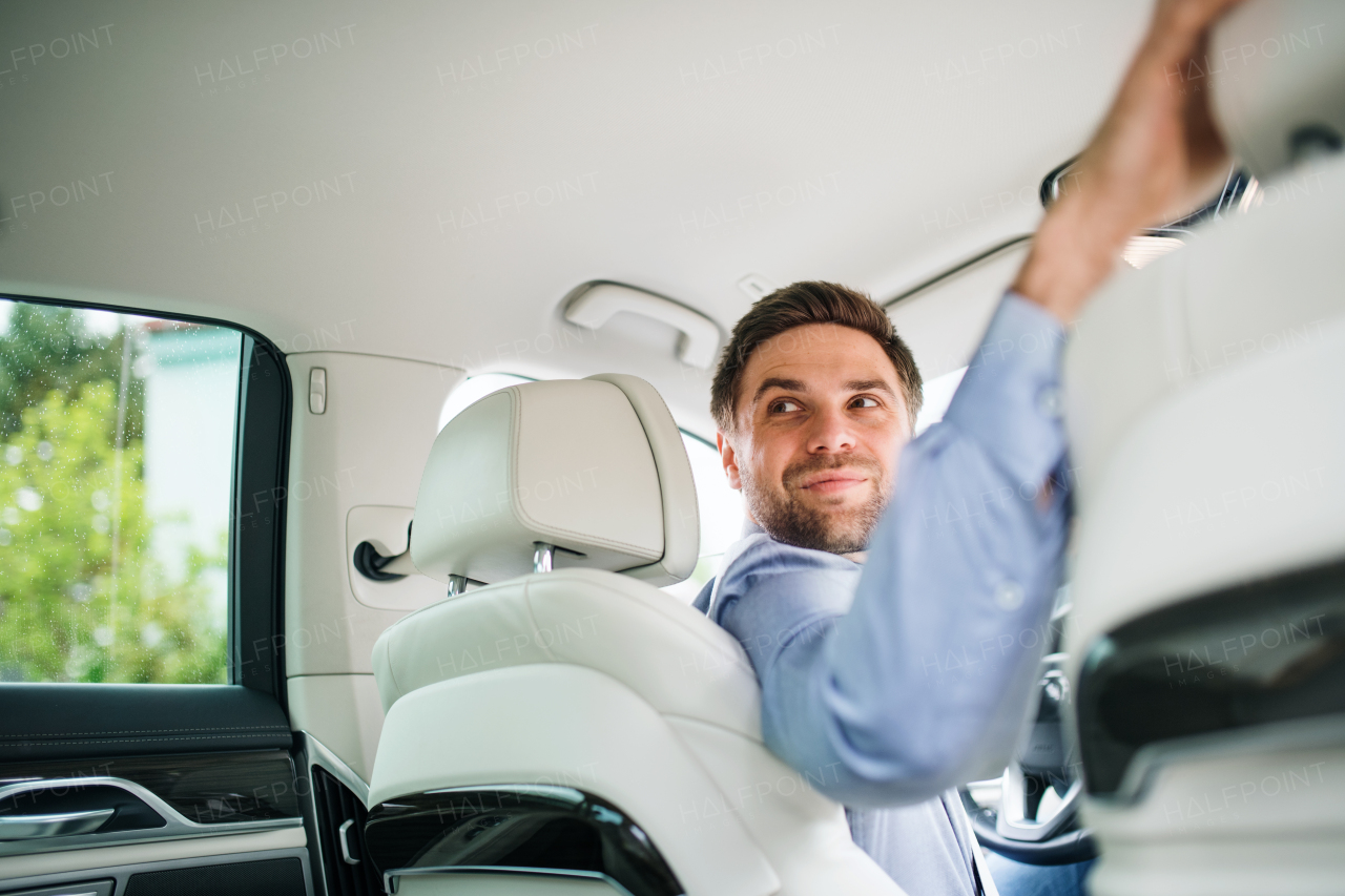 A businessman sitting in brand new car, looking back when driving.